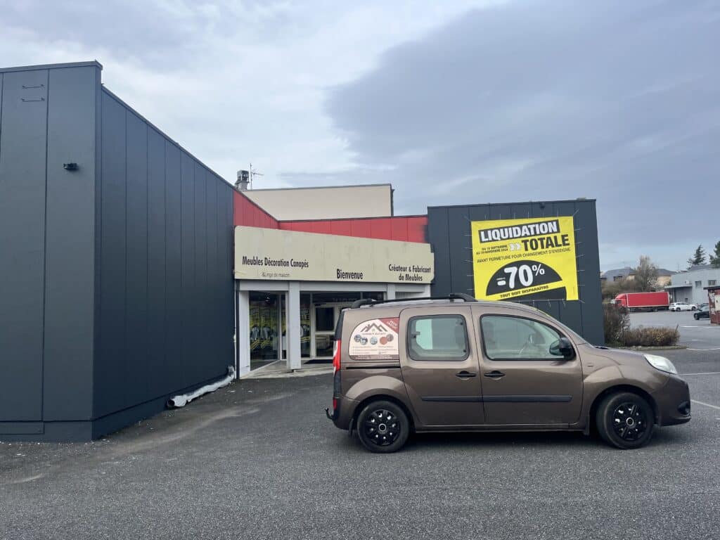 Liquidation totale -70% du magasin Meubles Décoration Canapés devant lequel stationne un utilitaire d'artisan.