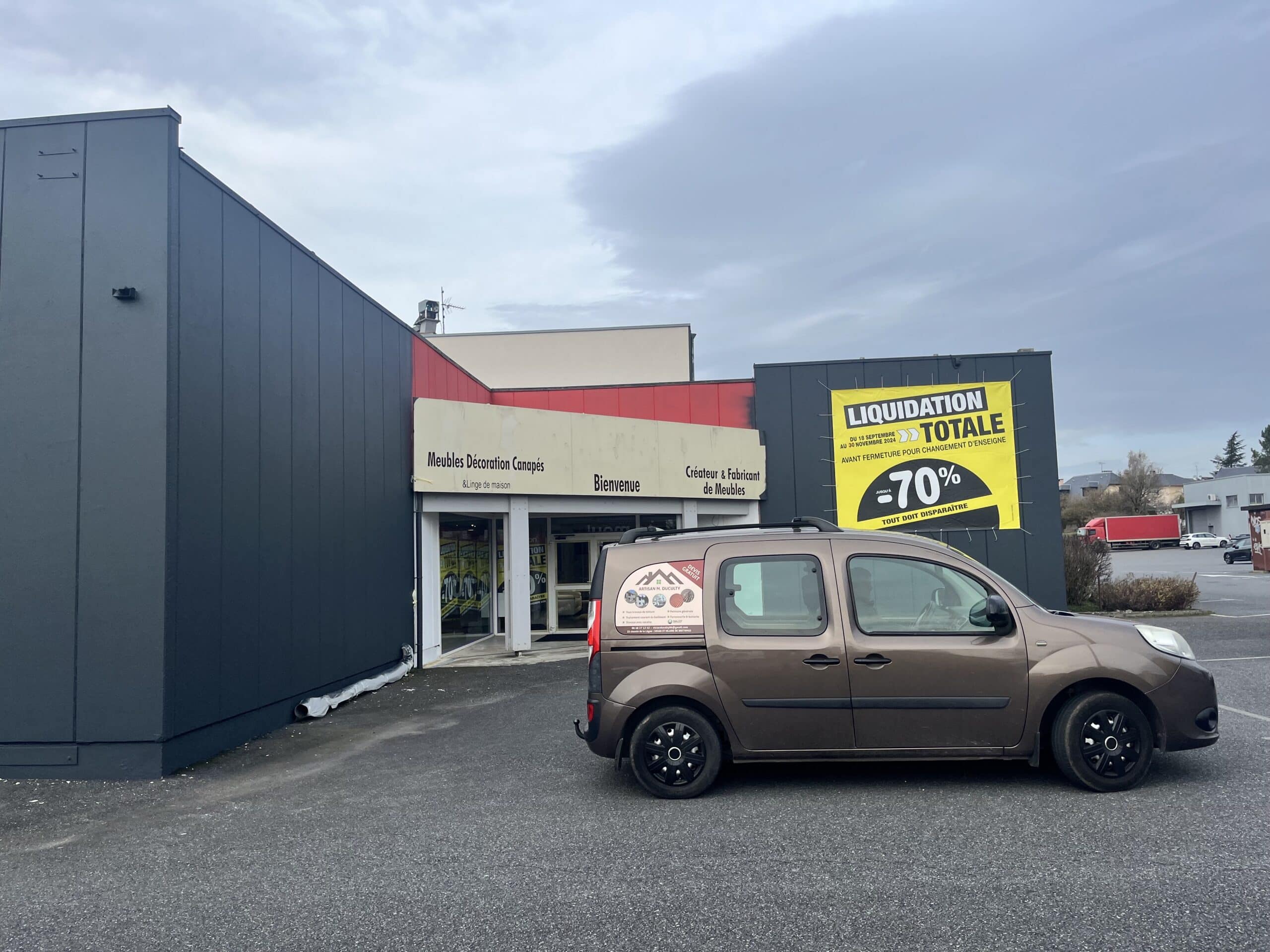 Liquidation totale -70% du magasin Meubles Décoration Canapés devant lequel stationne un utilitaire d'artisan.